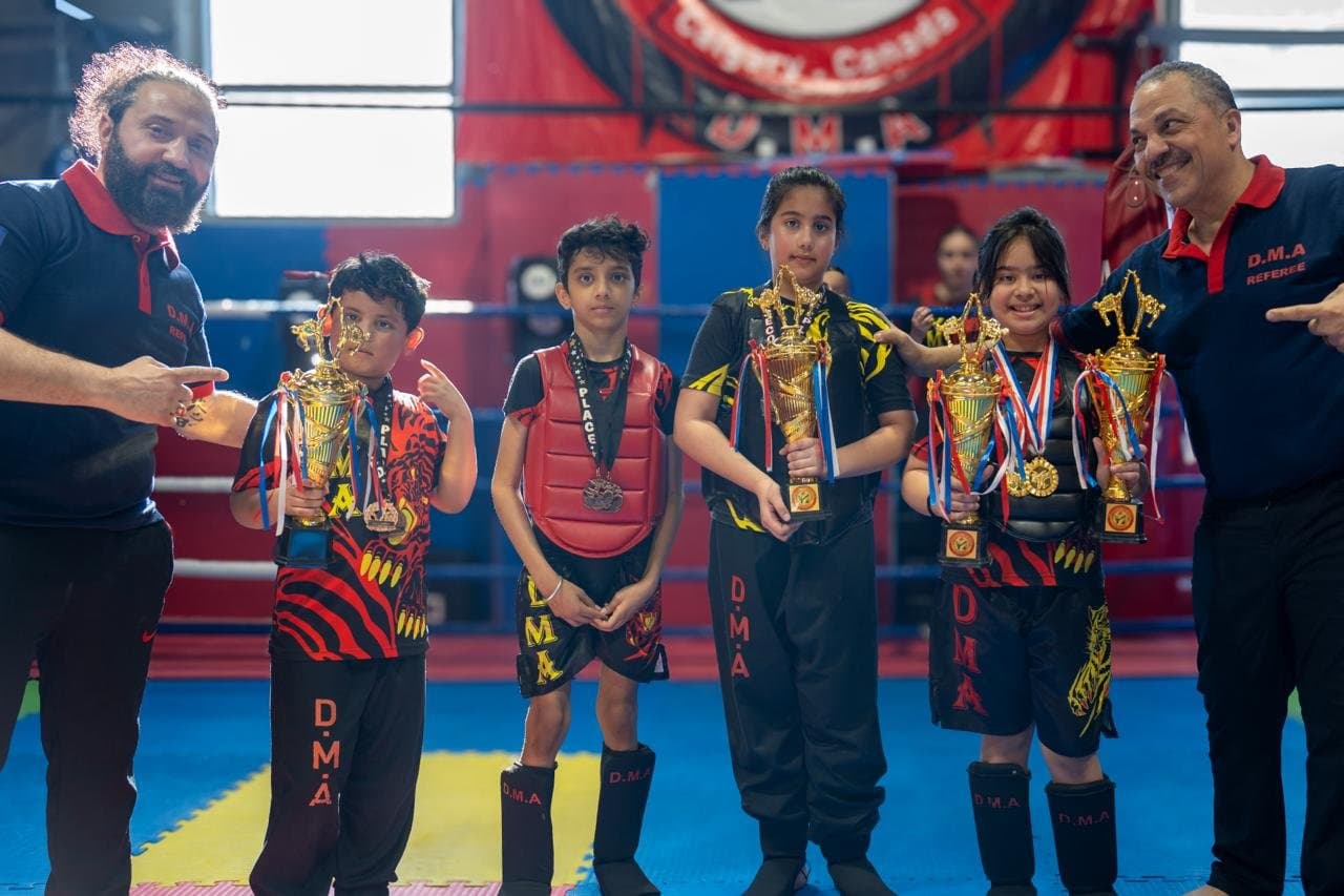 DMA coaches with young students proudly holding championship trophies and medals